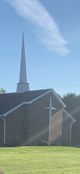 Faith Baptist Church brick exterior with a white steeple and cross beneath a clear blue sky.